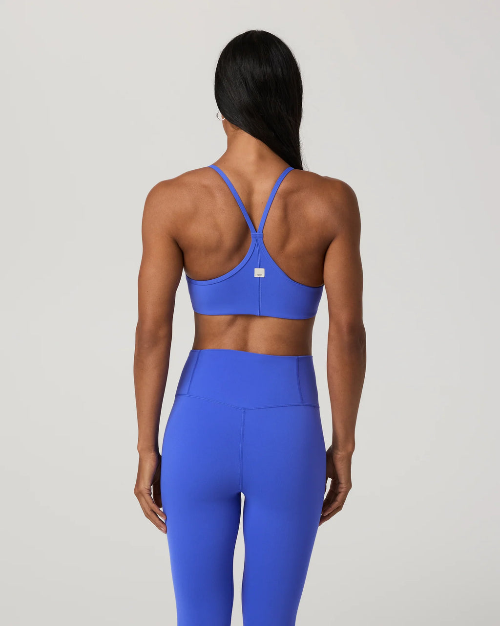 A woman shown from the back wearing a bright blue sports bra and matching high-waisted leggings against a light gray studio background.