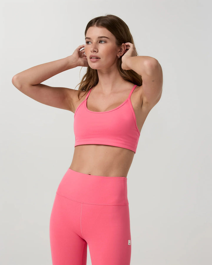 Woman wearing a pink sports bra and leggings on a light gray background