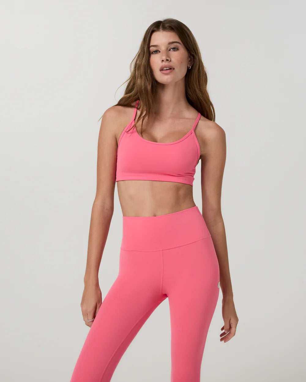 Woman wearing a pink sports bra and leggings on a light gray background