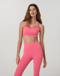Woman wearing a pink sports bra and leggings on a light gray background