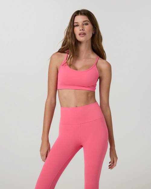 Woman wearing a pink sports bra and leggings on a light gray background