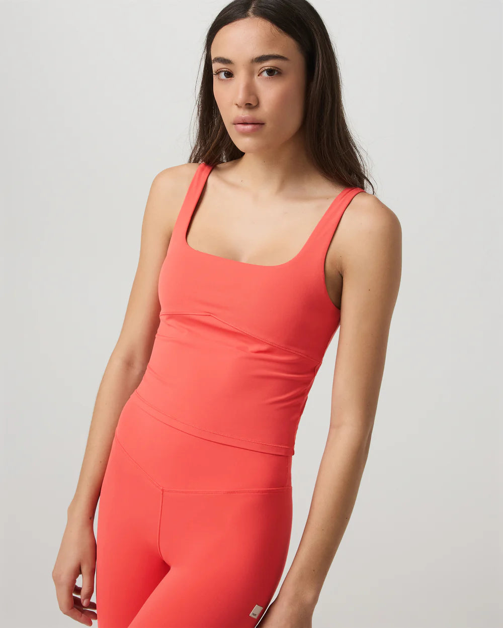Woman wearing a coral tank top and leggings on a light gray background