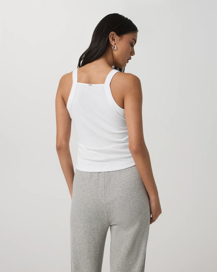 Woman wearing a white tank top and gray pants on a light gray background