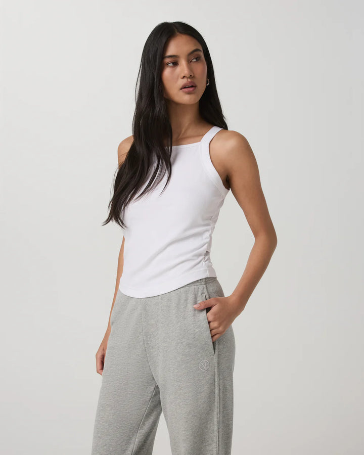 Woman wearing a white tank top and gray pants on a plain background