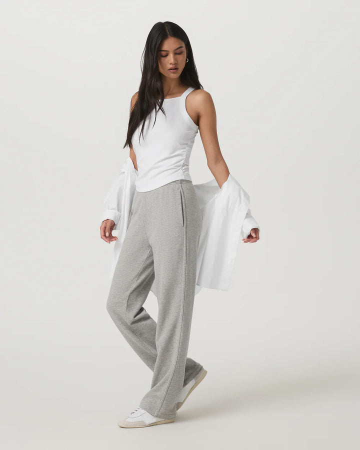 Woman wearing a white sleeveless top and gray pants on a white background