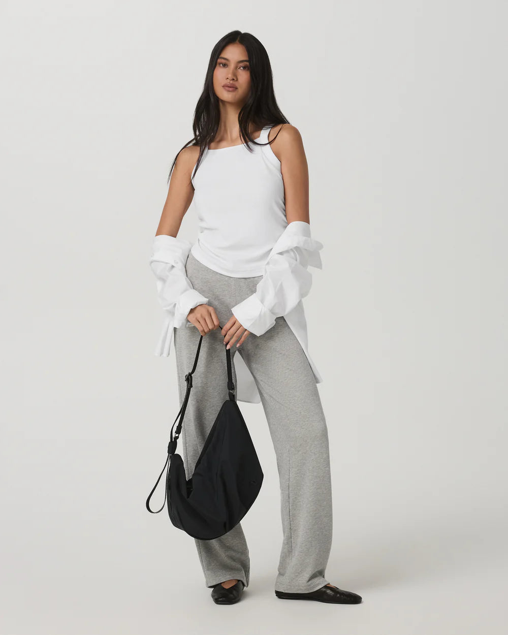 Woman wearing a white top and gray pants holding a black bag on a white background