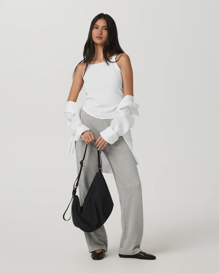 Woman wearing a white top and gray pants holding a black bag on a white background