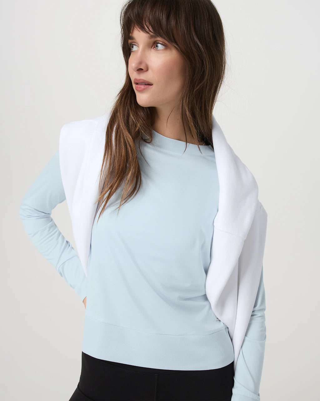 Woman wearing a light blue long-sleeve top with a white cardigan on a plain background