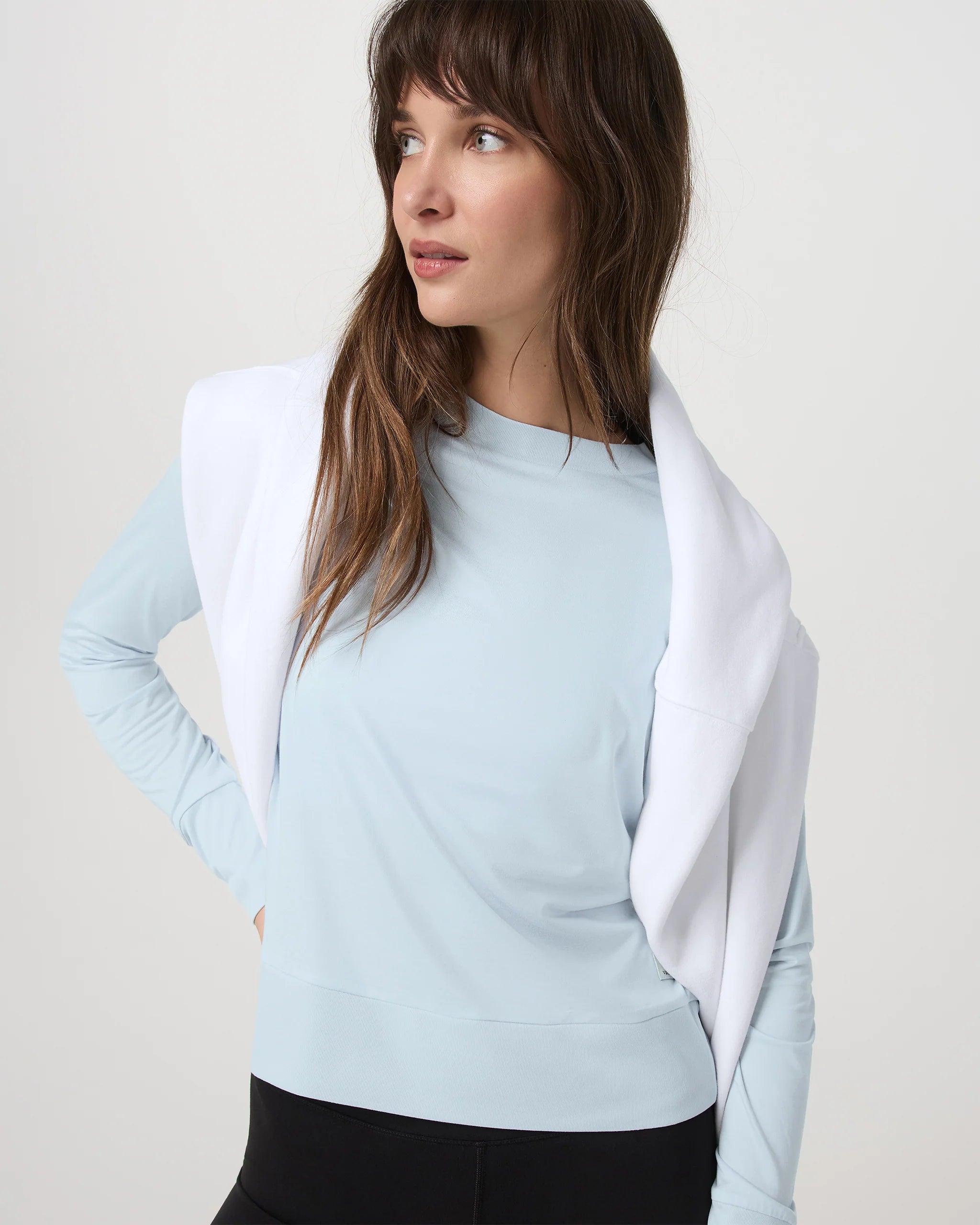 Woman wearing a light blue long-sleeve top with a white cardigan on a plain background