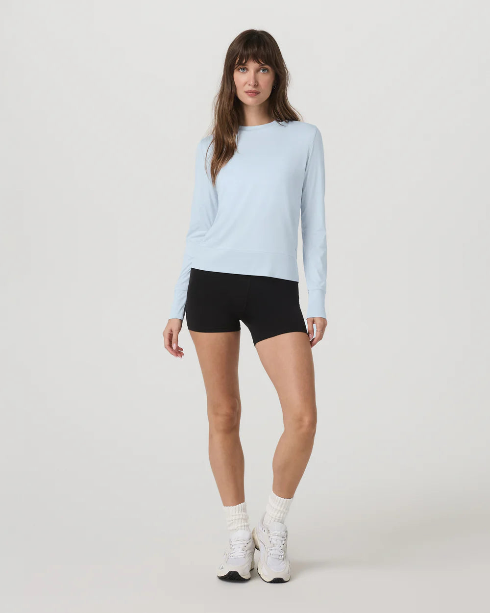 Woman wearing a light blue long-sleeve top and black shorts on a white background