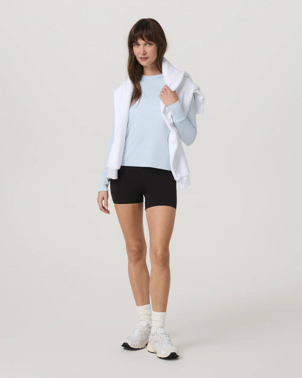 Woman wearing a light blue sweater, black shorts, white sneakers, and a white jacket on a white background