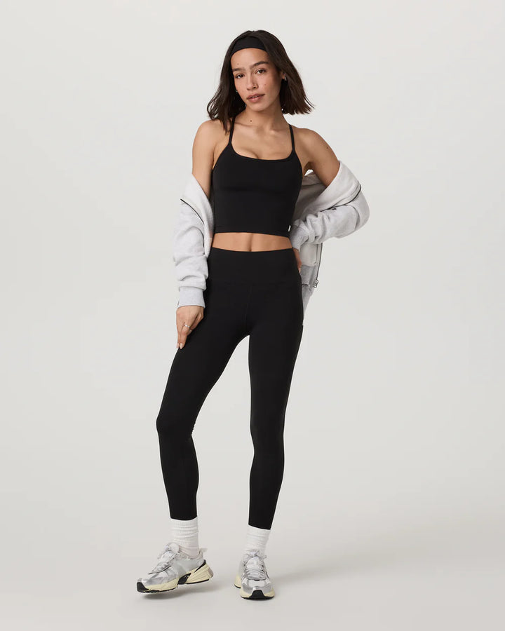 Woman wearing a black sports bra and leggings with a light gray jacket on a white background