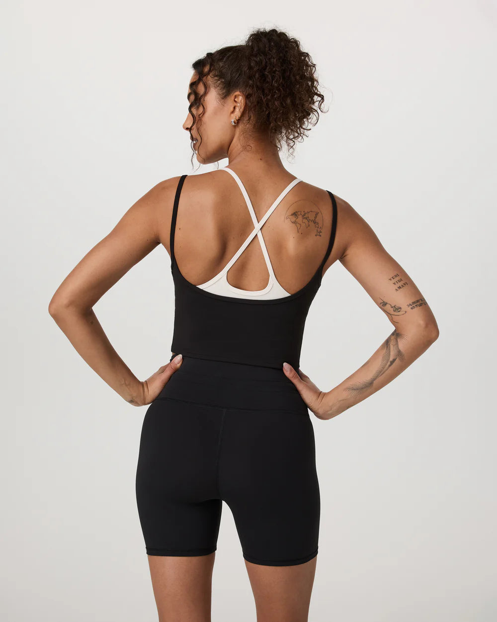 Person wearing a black athletic outfit with white straps on a plain background