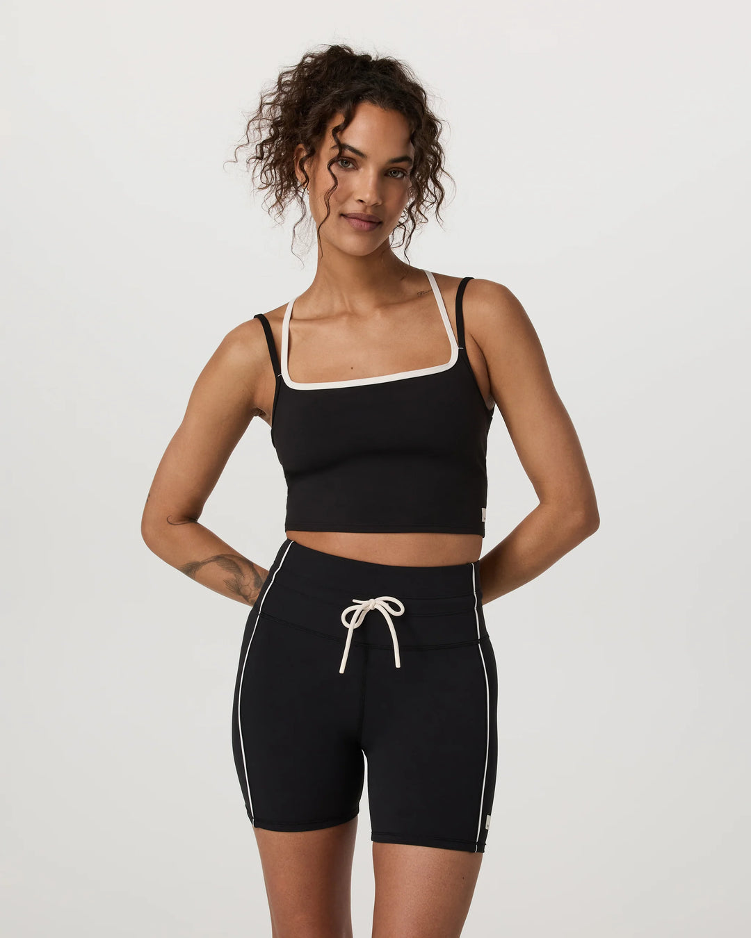 Woman wearing a black sports bra and shorts with white trim on a light gray background