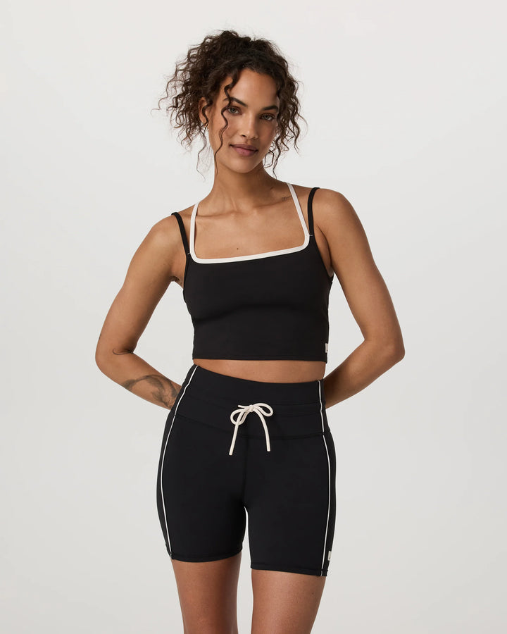 Woman wearing a black sports bra and shorts with white trim on a light gray background