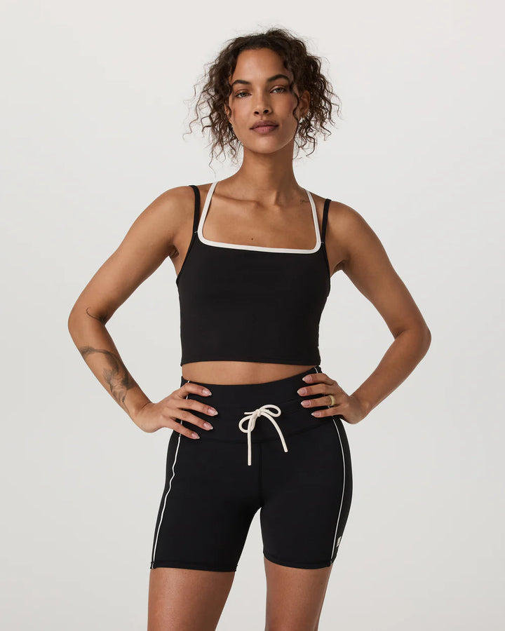 Woman wearing a black sports bra and shorts with white trim on a light gray background