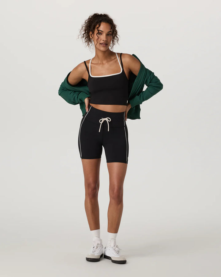 Woman wearing a black sports bra and shorts with a green cardigan on a white background