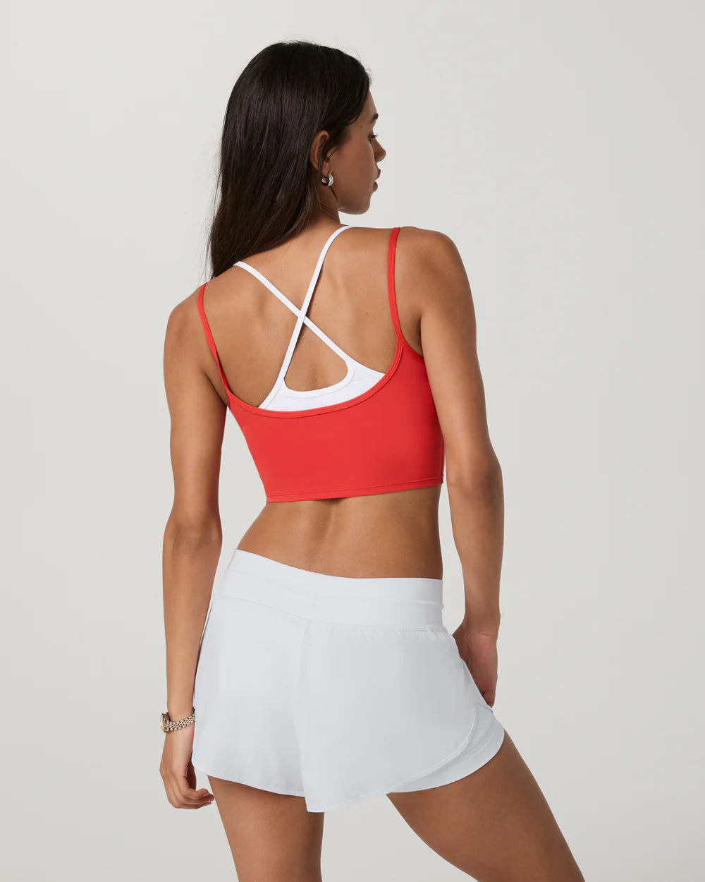 Woman wearing a red sports bra and white shorts on a plain background