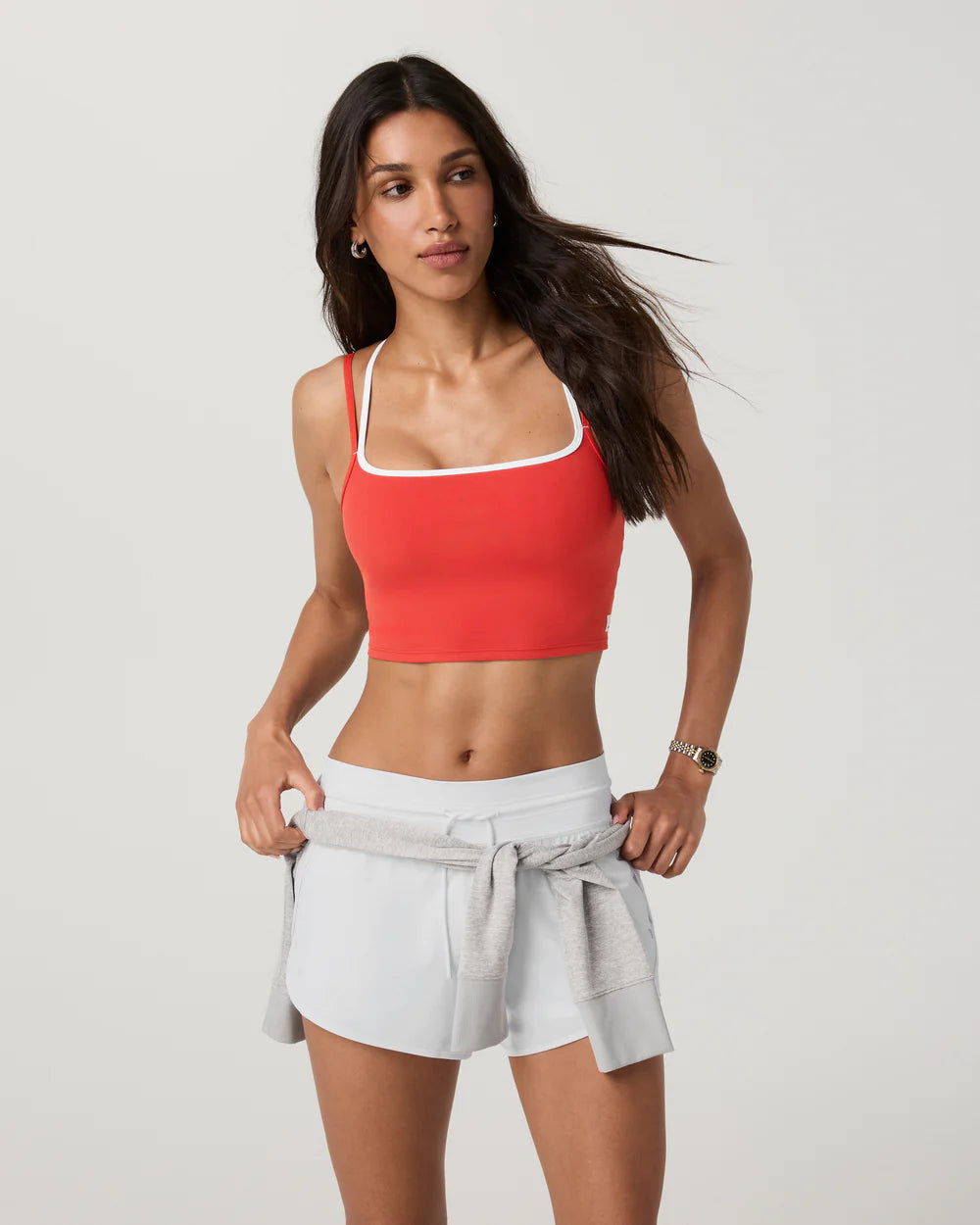 Woman wearing a red sports bra and gray shorts on a white background