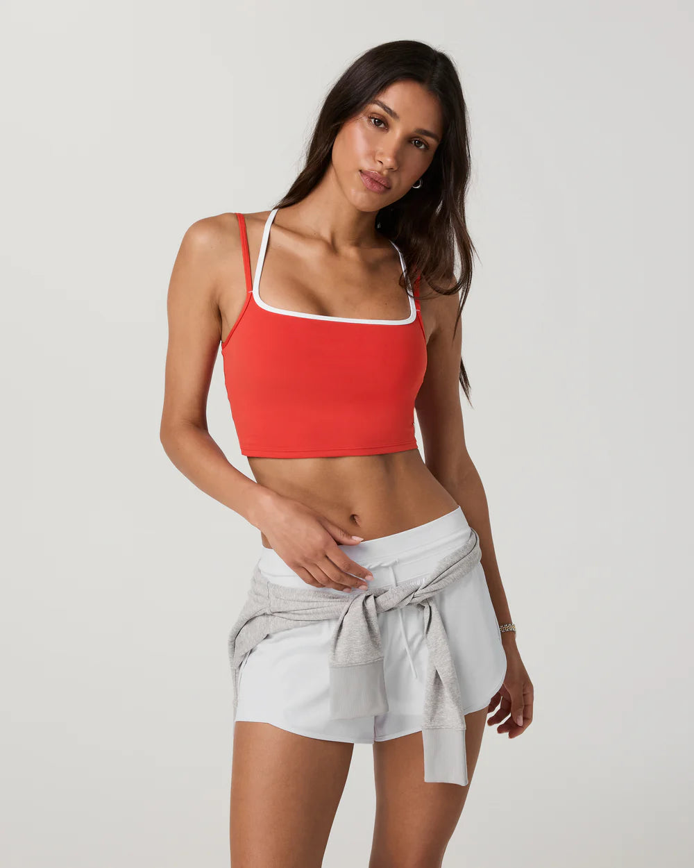 Woman wearing a red sports bra and light gray shorts on a white background