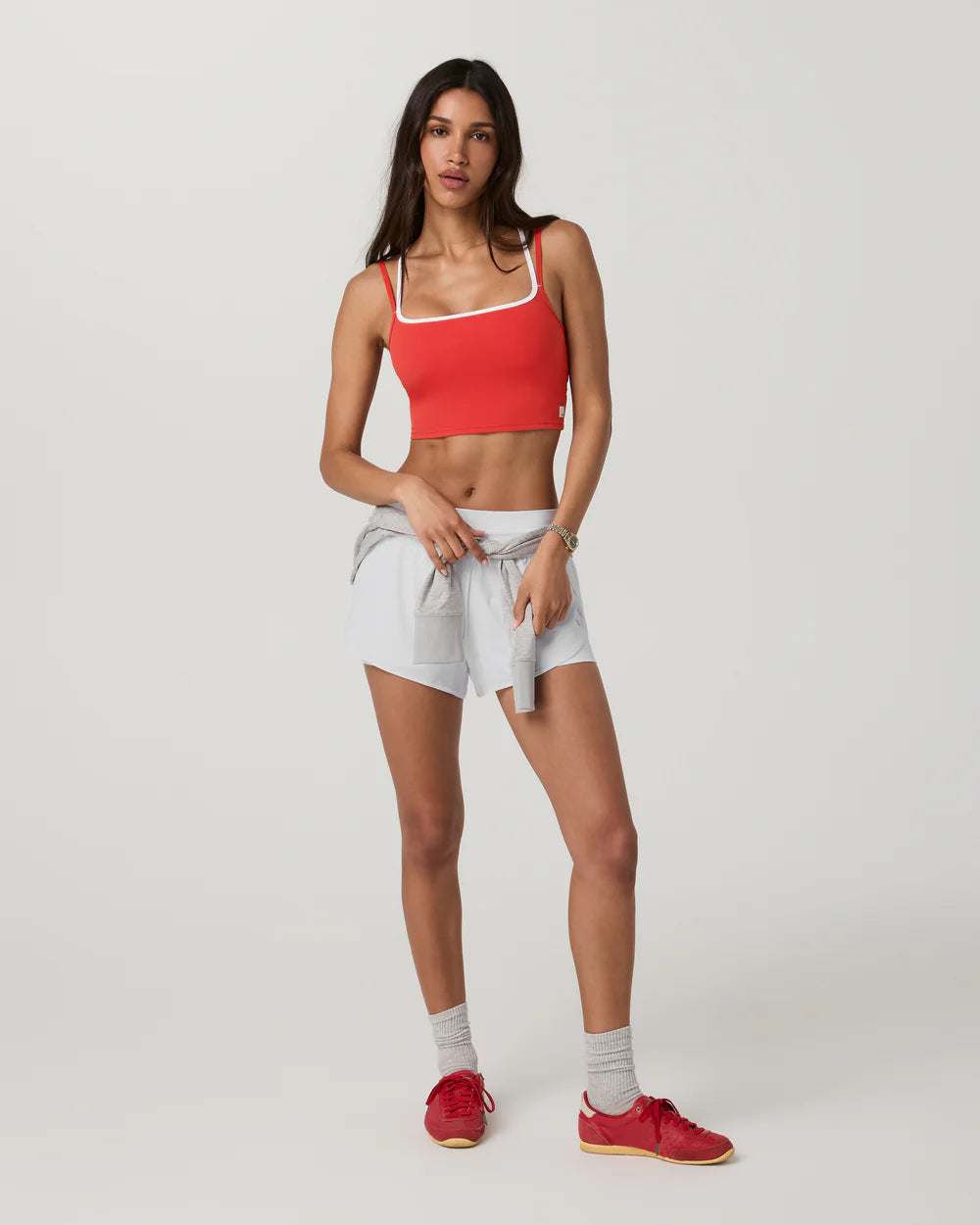 Woman wearing a red sports bra and white shorts on a plain background