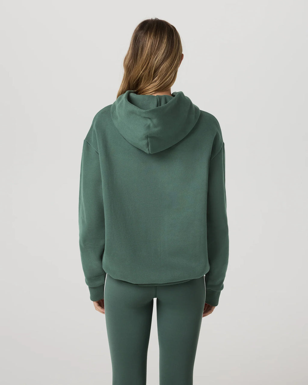 Person wearing a green hoodie and pants on a light gray background