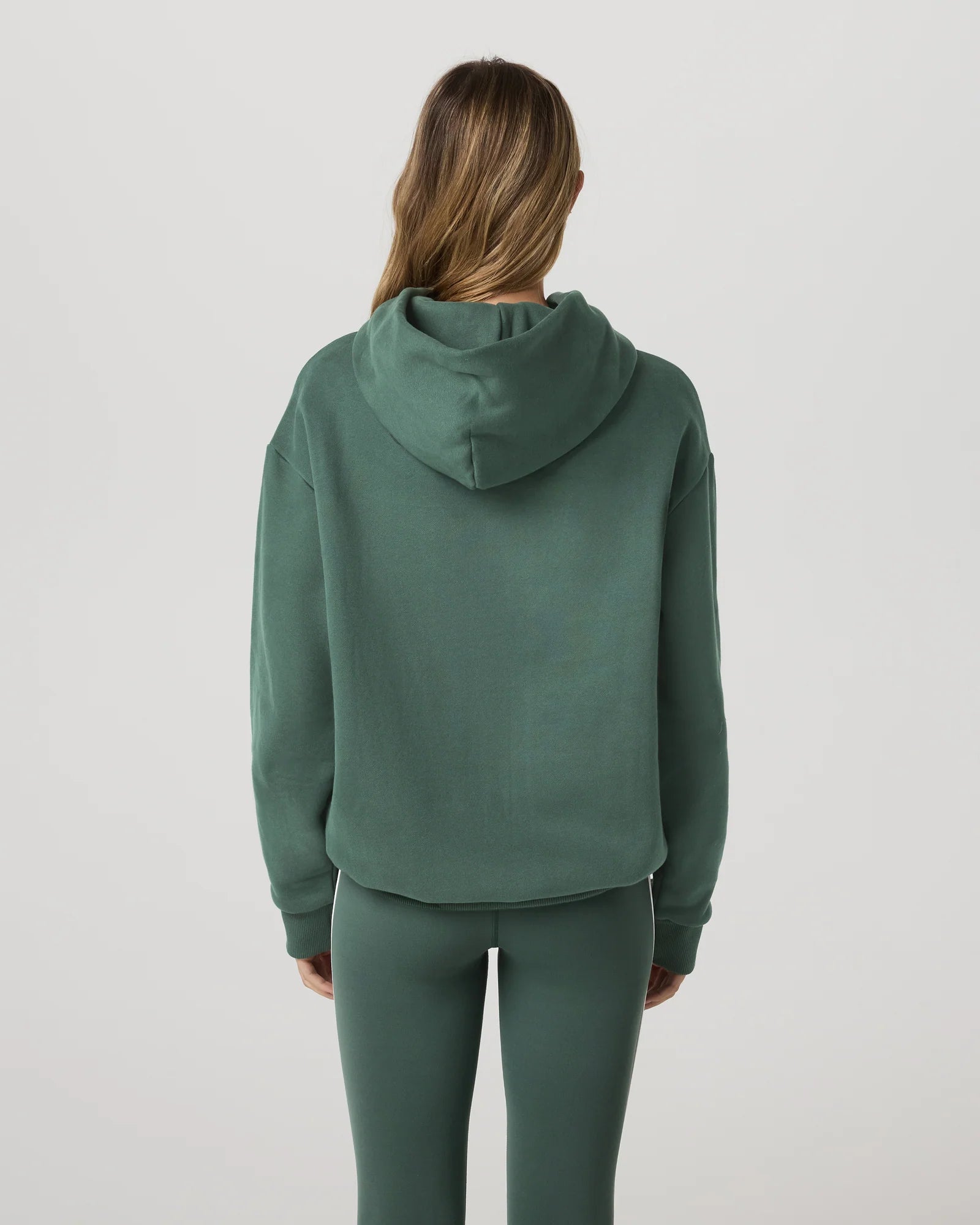 Person wearing a green hoodie and pants on a light gray background