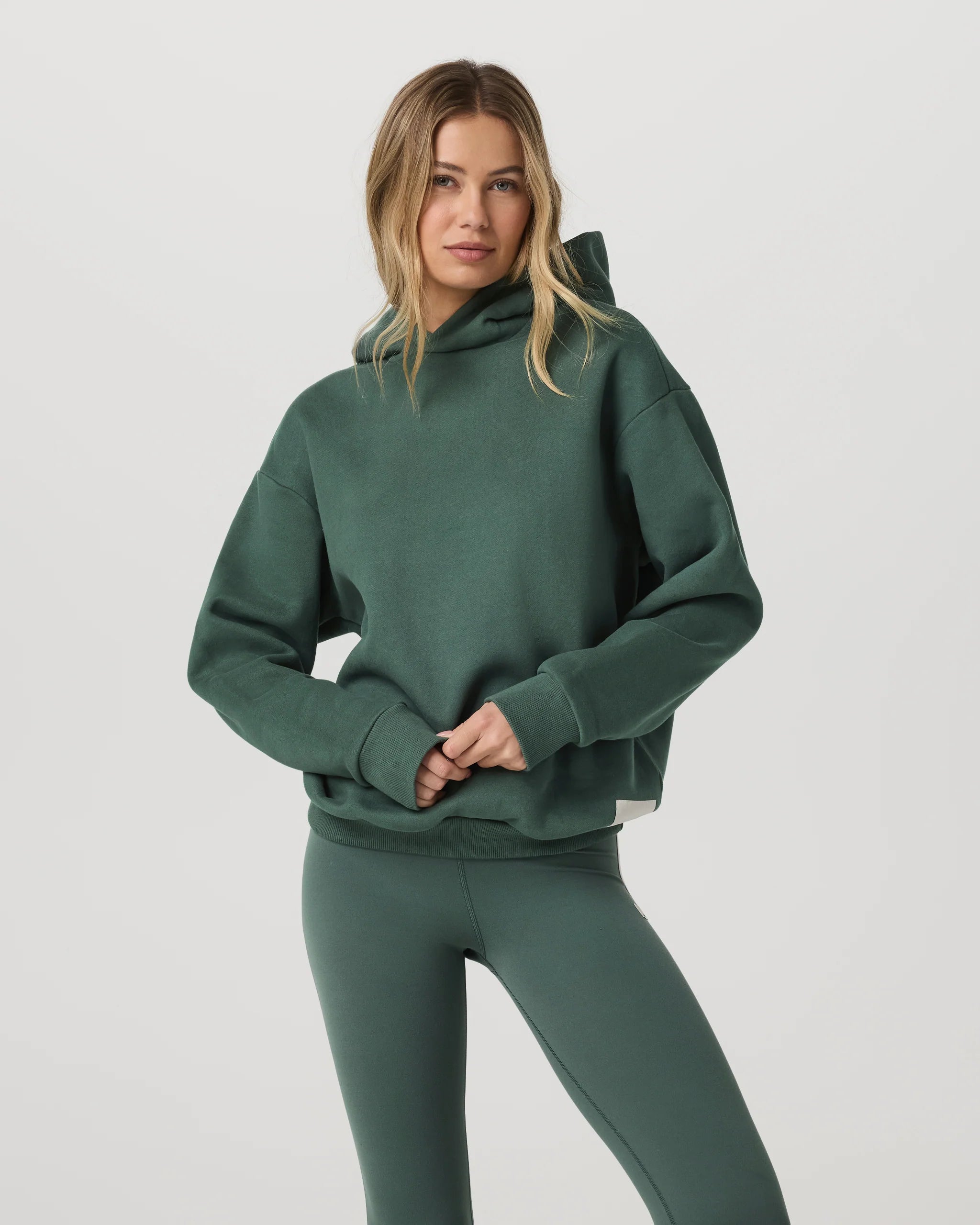 Woman wearing a green hoodie and leggings on a light gray background