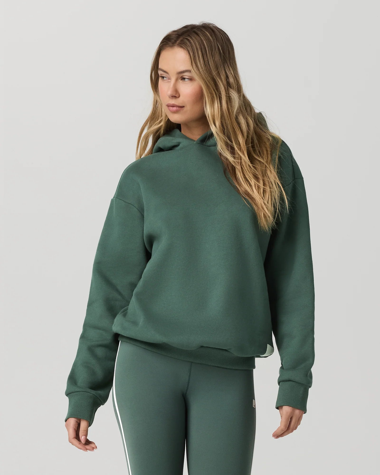 Woman wearing a green hoodie and leggings on a plain background