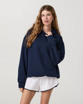 A woman modeling an oversized navy blue hoodie with white athletic shorts against a light gray studio background.