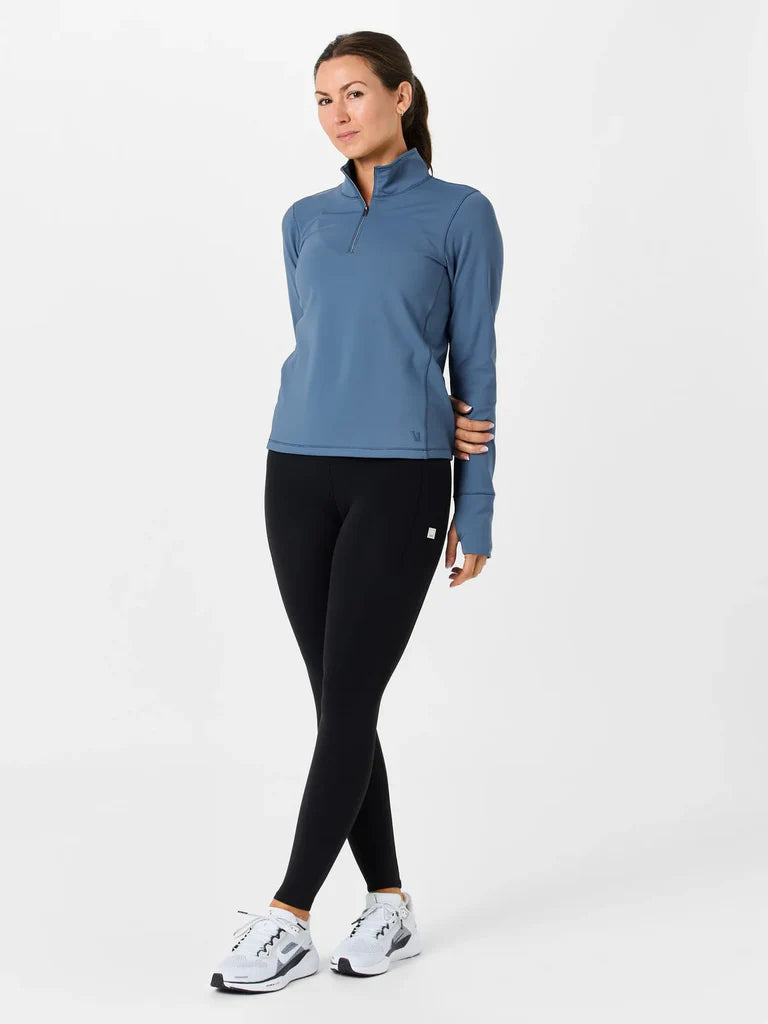 Woman wearing a blue long-sleeve top and black leggings on a white background