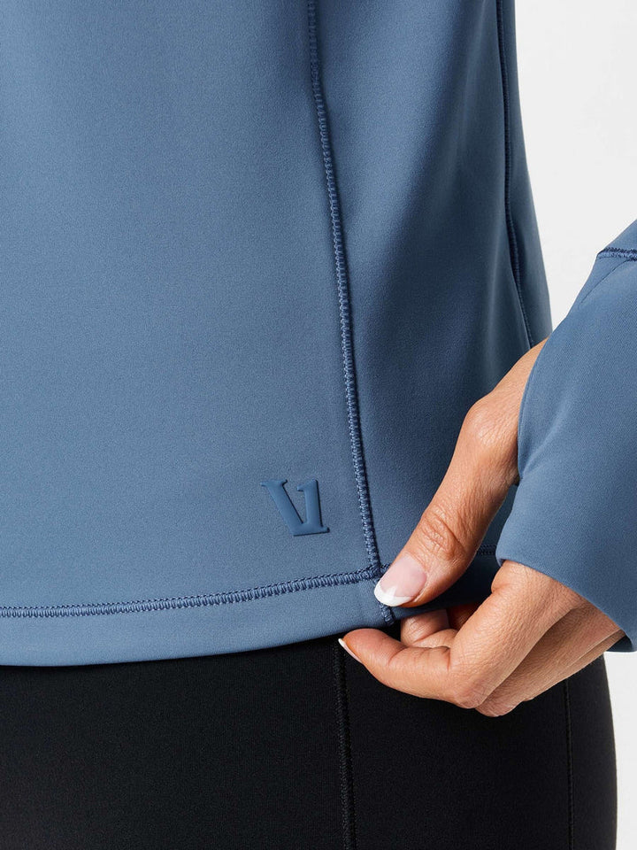 Close-up of a person wearing a blue jacket with a brand logo, holding the sleeve.