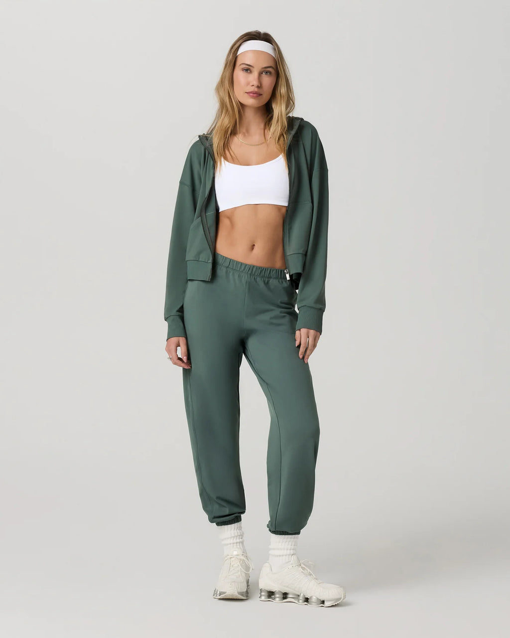 Woman wearing a green tracksuit with a white top on a light gray background