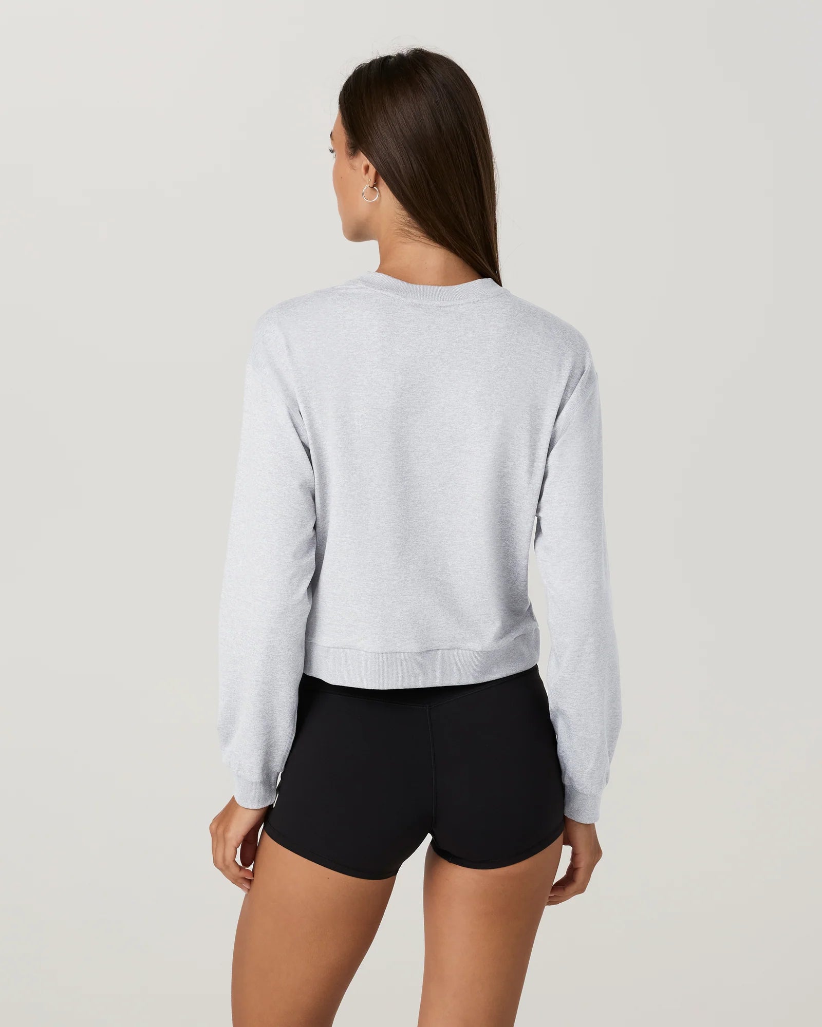 Person wearing a light gray sweatshirt and black shorts on a plain background