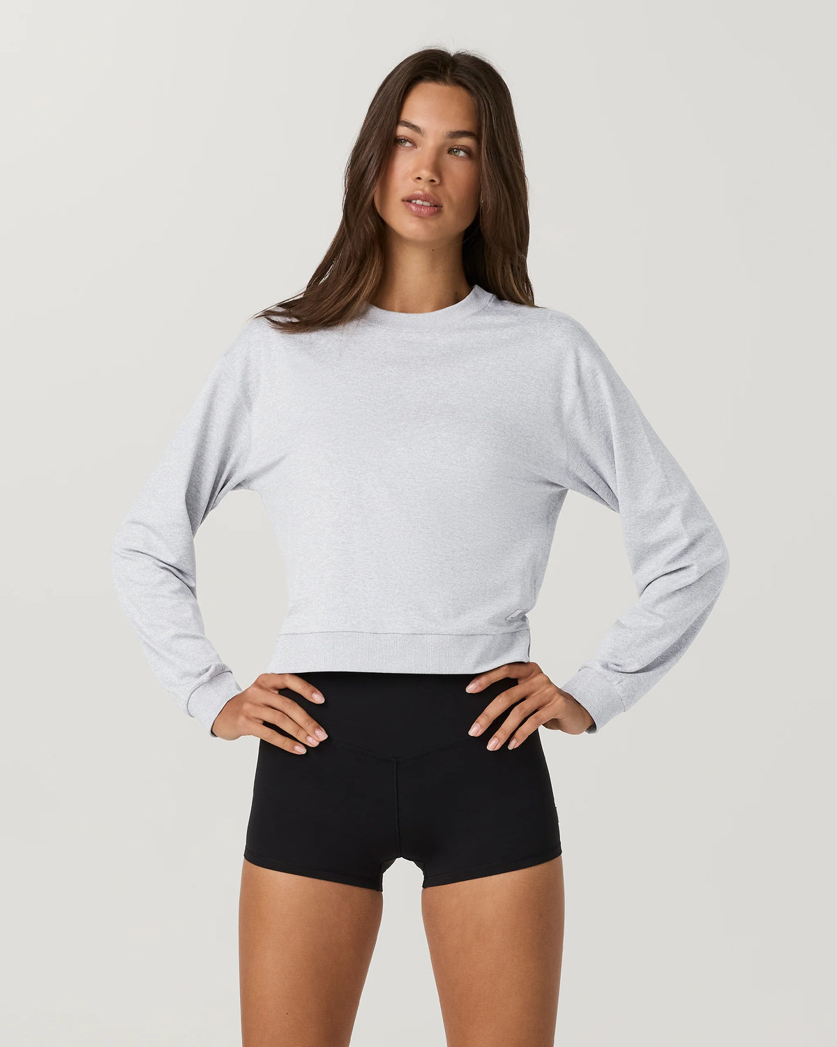 Woman wearing a light gray cropped sweatshirt and black shorts on a plain background