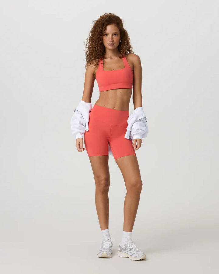 Woman wearing a coral sports bra and shorts set on a white background