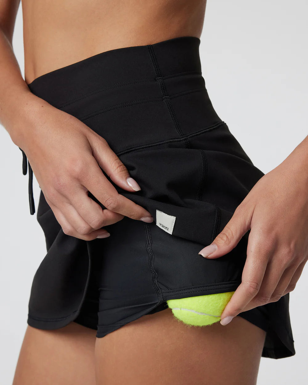 Person wearing a black athletic skirt holding a tennis ball.