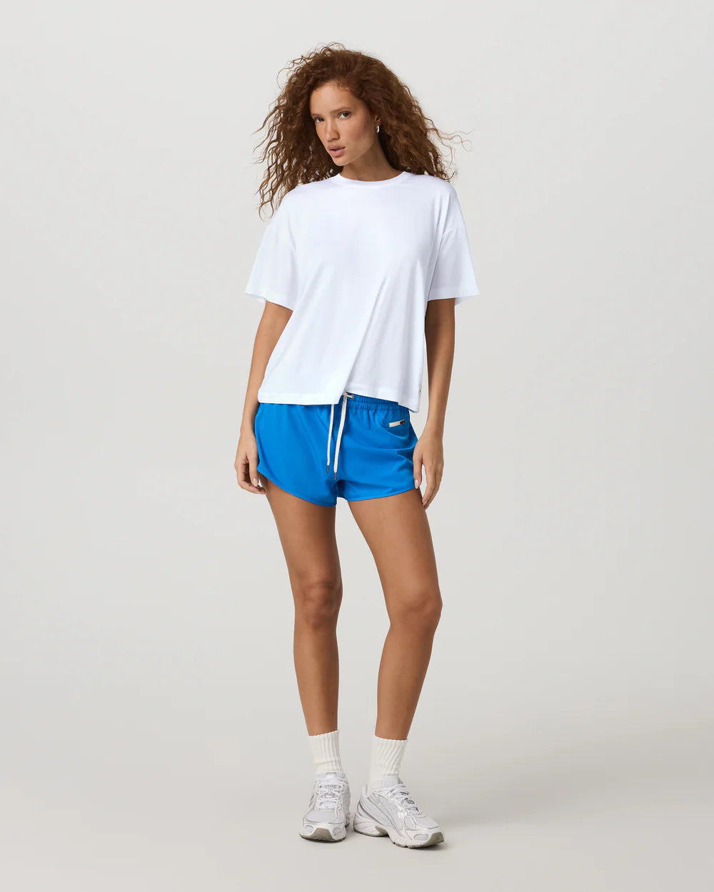 Woman wearing a white t-shirt and blue shorts on a plain background