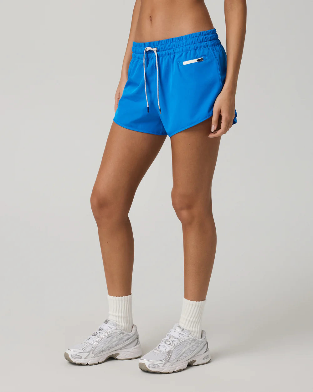 Person wearing blue shorts and white sneakers on a plain background