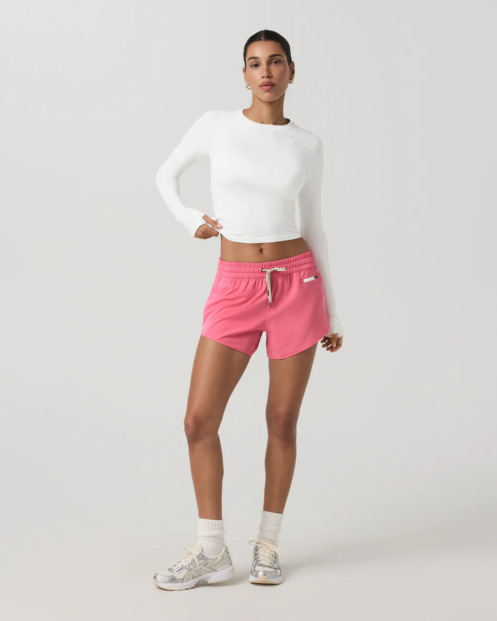 Woman wearing a white long-sleeve top and pink shorts on a light gray background
