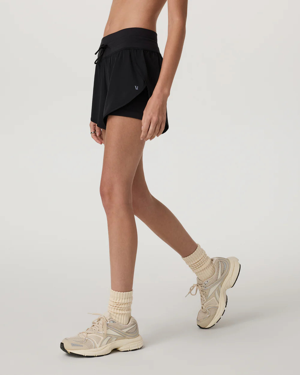 Person wearing black shorts, beige sneakers, and socks on a light gray background