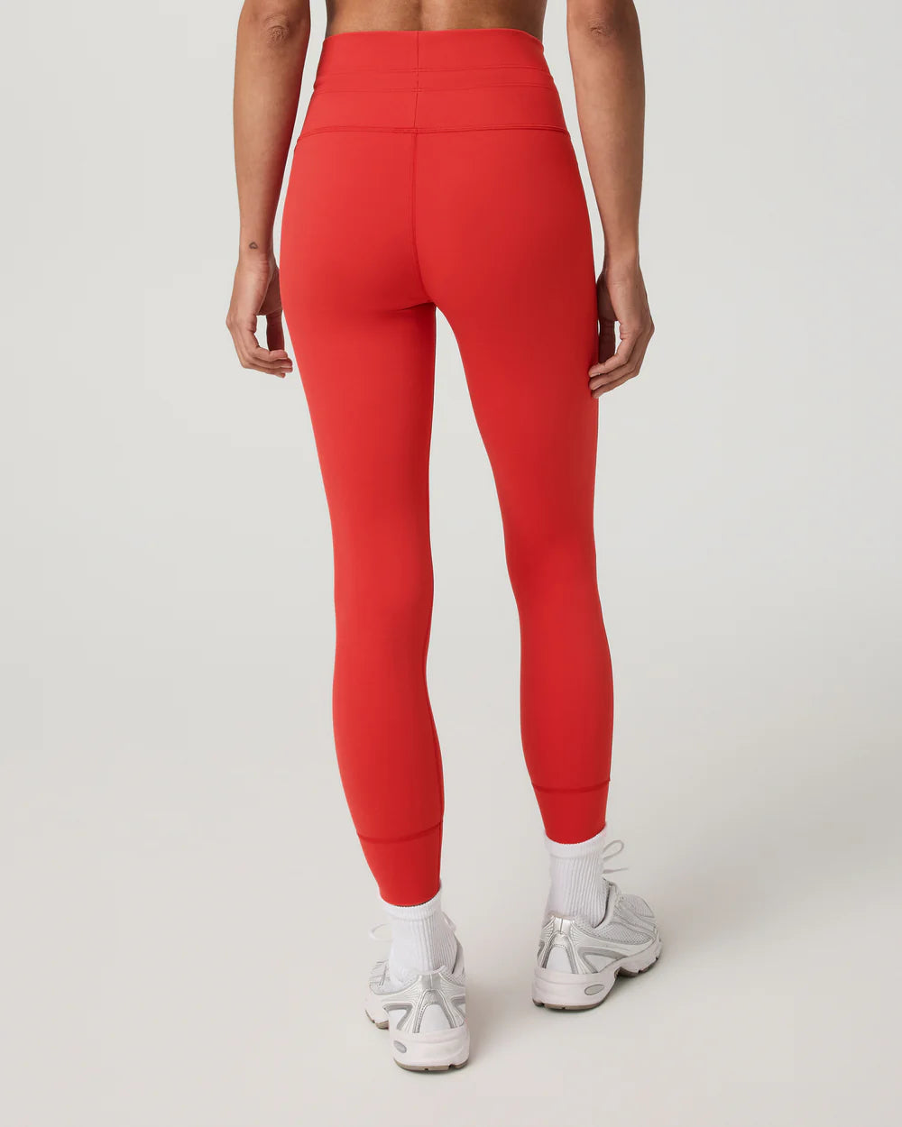 A model shown from the back wearing bright red high-waisted leggings, white socks, and white sneakers against a light gray studio background.