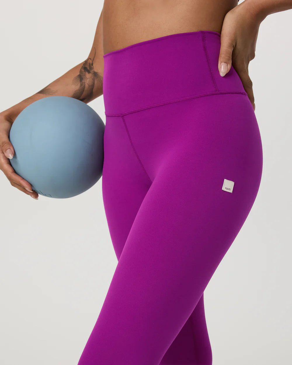 Person wearing purple leggings holding a blue ball on a plain background