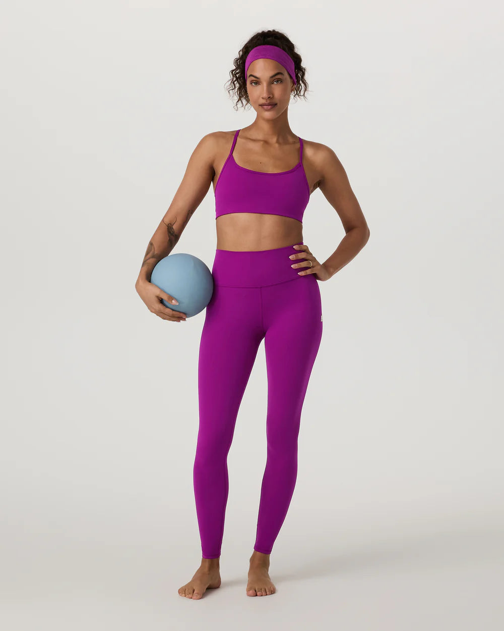 Woman in purple athletic wear holding a blue ball on a white background