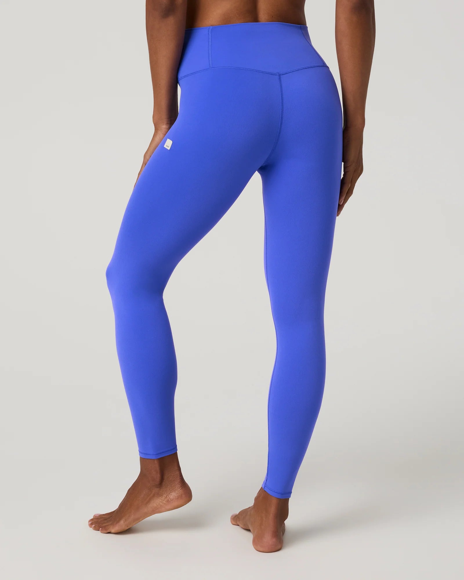 A model from the back wearing bright royal blue high-waisted leggings, standing barefoot against a light gray studio background.