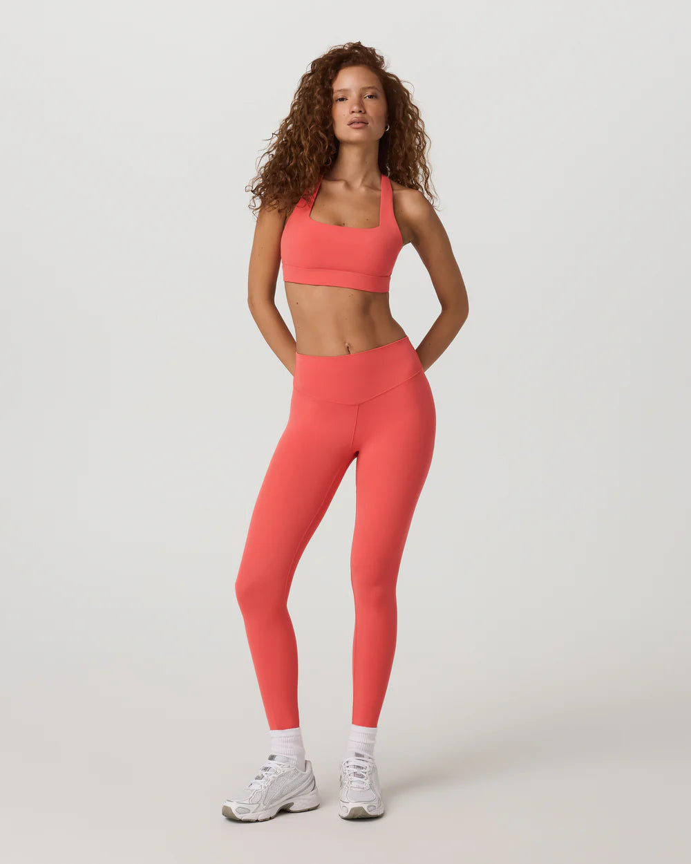 Woman wearing a coral sports bra and leggings set on a white background