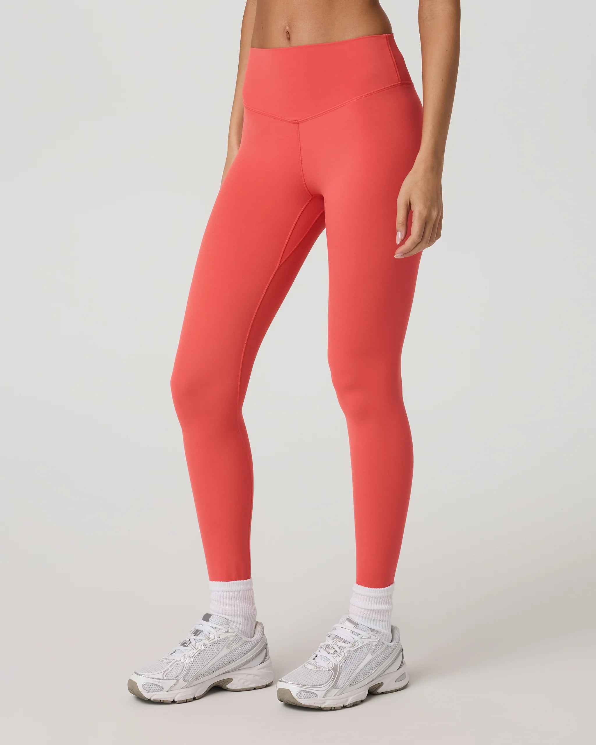 Person wearing coral leggings and white sneakers on a light gray background