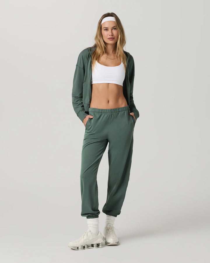 Woman wearing a green tracksuit and white sneakers on a light gray background