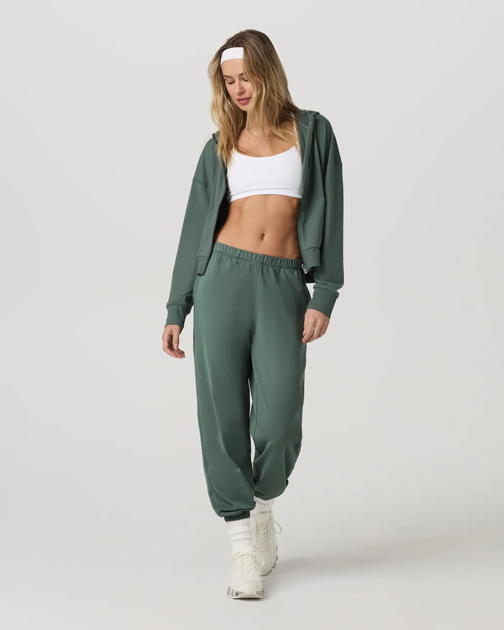 Woman wearing a green tracksuit with a white top on a light gray background