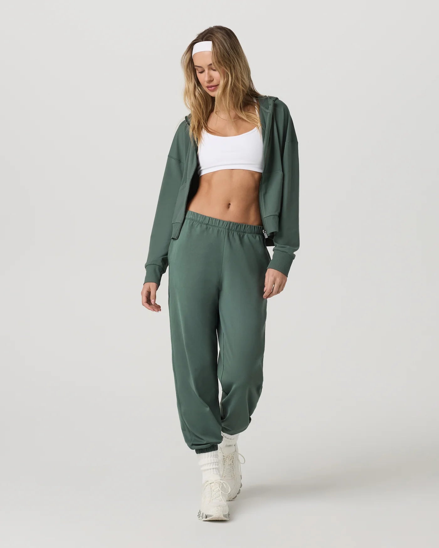 Woman wearing a green tracksuit with a white top on a light gray background